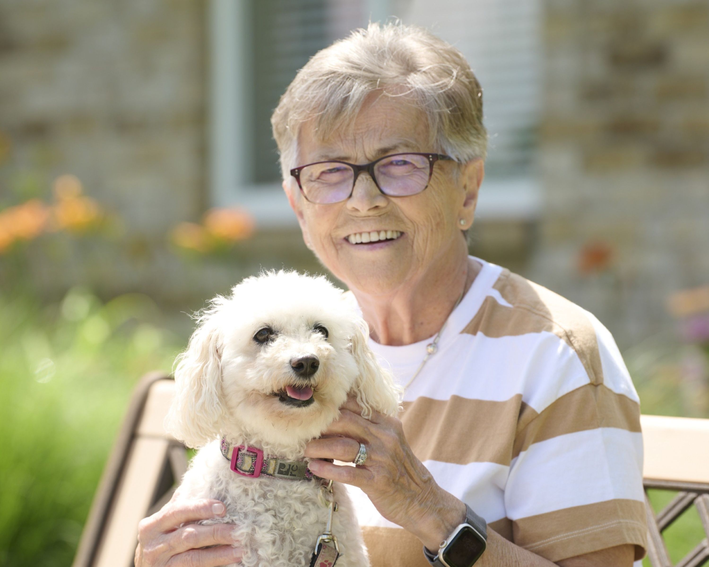 Older woman with glasses holding white poodle.